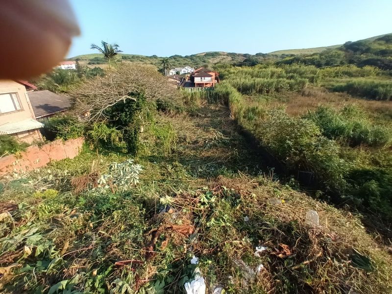 An elevated view of a vacant residential plot featuring sloped terrain and cleared vegetation, situated in a suburban neighborhood.