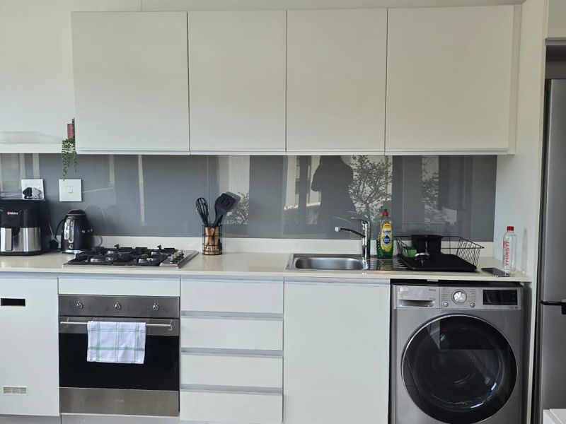 Modern kitchen featuring white cabinetry, glass splashback, gas hob, built-in oven, and integrated laundry appliance.