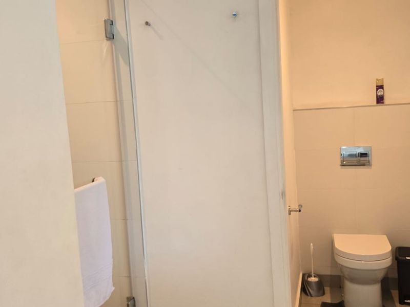 A clean, functional bathroom featuring a wall-mounted toilet with a concealed cistern and a separate shower enclosure with tiled walls.