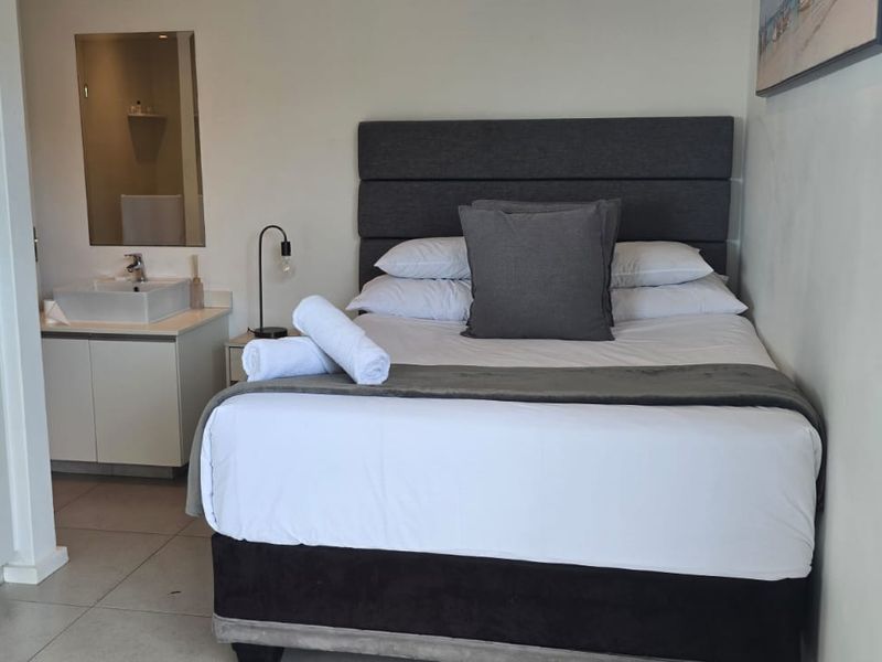 A compact bedroom featuring a built-in wardrobe and an integrated vanity basin area with tiled flooring.