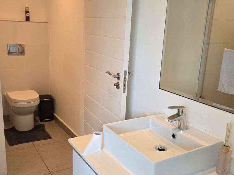 A modern bathroom featuring a wall-hung toilet with a concealed cistern, a vessel sink vanity, and a large wall mirror.