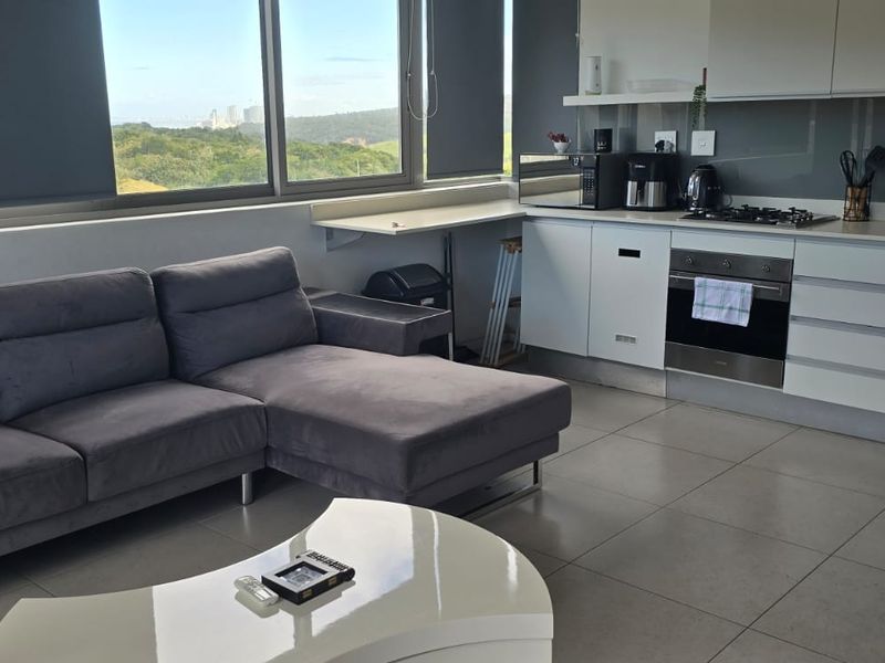 Modern open-plan living area featuring a sleek kitchen with built-in appliances, tiled flooring, and large windows offering scenic views.
