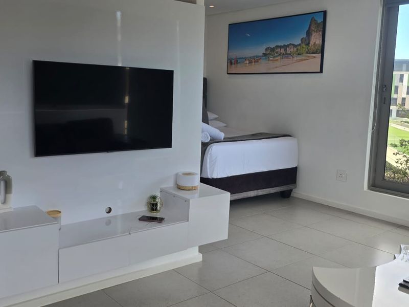 Modern bedroom featuring tiled flooring, a built-in media console, and a large sliding glass door providing natural light and exterior views.