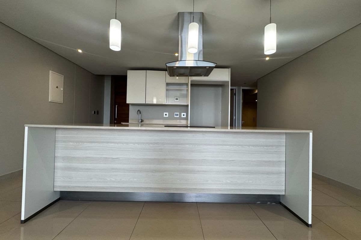 Modern open-plan kitchen featuring a central island, sleek cabinetry, stainless steel extractor fan, and neutral tiled flooring in a well-maintained apartment space.