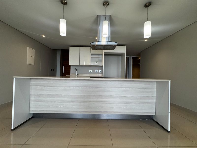 Modern open-plan kitchen featuring a central island, sleek cabinetry, stainless steel extractor fan, and neutral tiled flooring in a well-maintained apartment space.