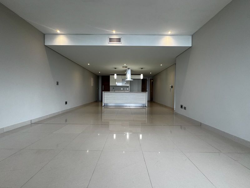 Spacious open-plan living and kitchen area featuring polished porcelain floor tiles, modern recessed lighting, and a central kitchen island with an integrated extractor fan.