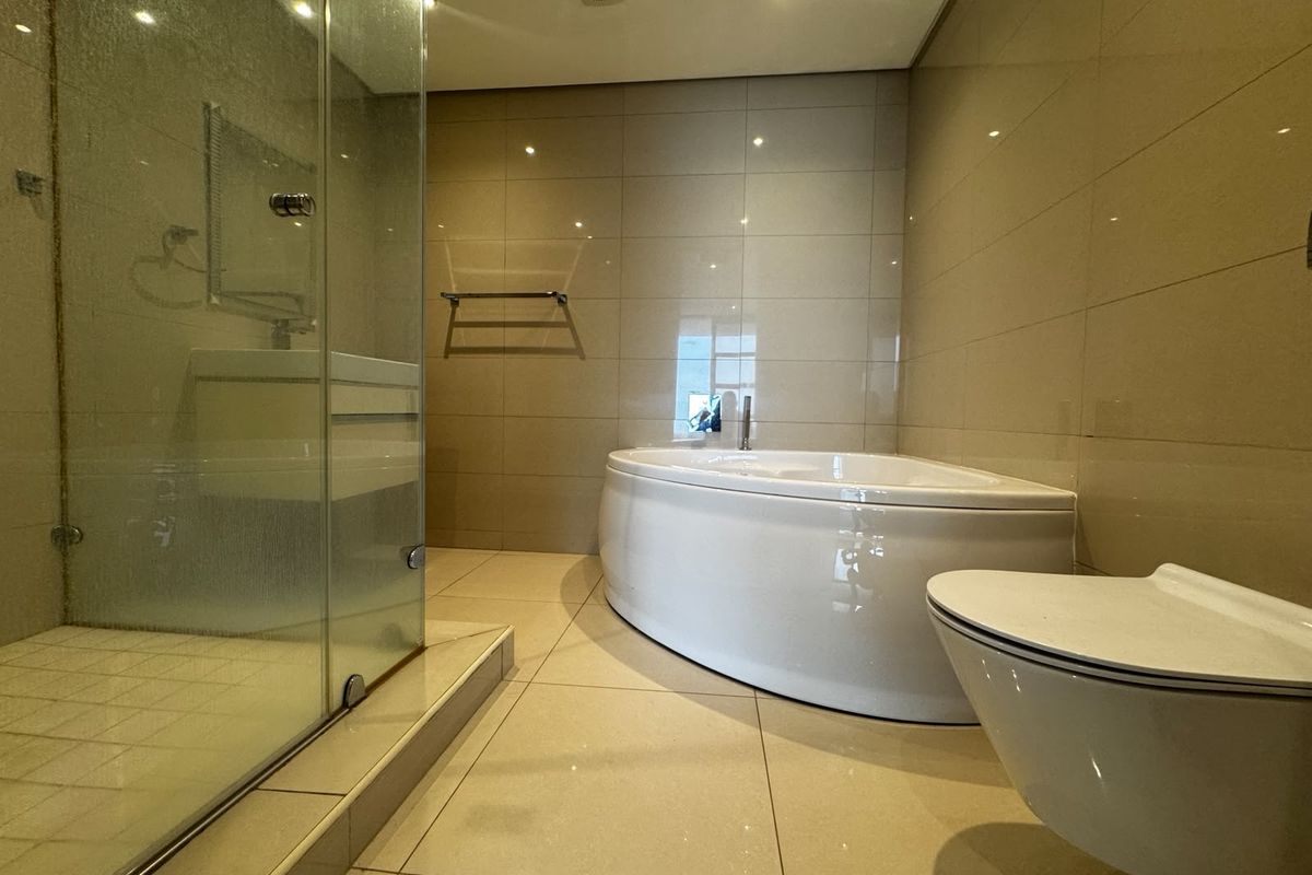 Modern bathroom featuring a glass shower enclosure, a curved built-in bathtub, and a wall-mounted toilet with neutral floor-to-ceiling tiling.