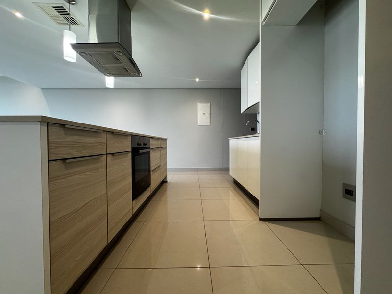 Modern kitchen featuring a central island, built-in oven, extractor fan, and sleek cabinetry with neutral tiled flooring.