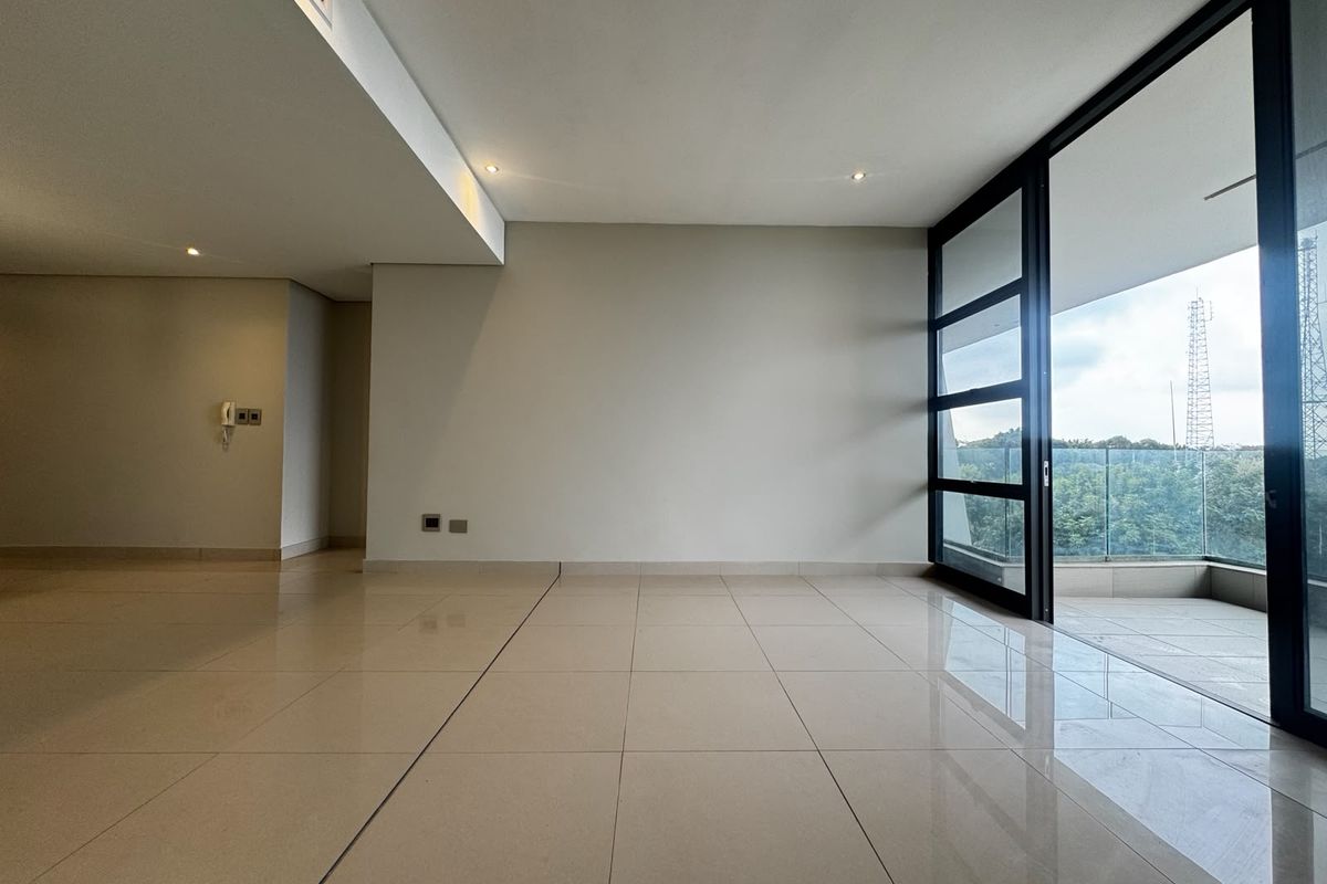 A bright, empty living area featuring large sliding glass doors that open onto a balcony with a glass balustrade and tiled flooring throughout.