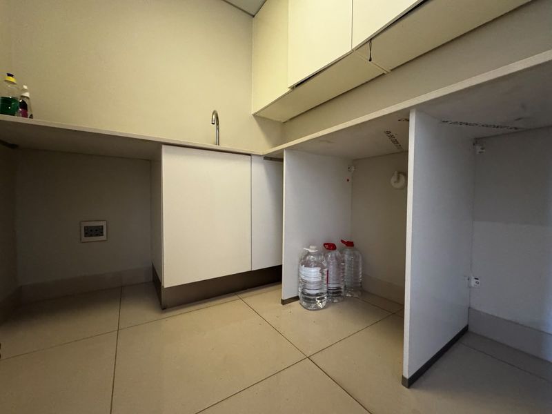 A functional laundry area featuring built-in cabinetry, a countertop with a sink faucet, and tiled flooring with dedicated plumbing connections for appliances.