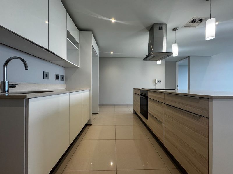 Modern kitchen featuring sleek white and wood-grain cabinetry, stone countertops, a central island with built-in oven, and high-quality stainless steel fixtures.