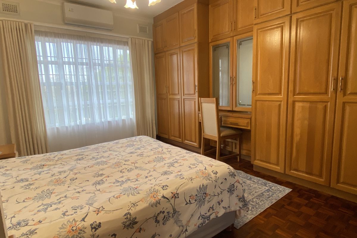 A bedroom featuring extensive built-in wooden cabinetry with an integrated vanity, parquet flooring, and a wall-mounted split-system air conditioner.