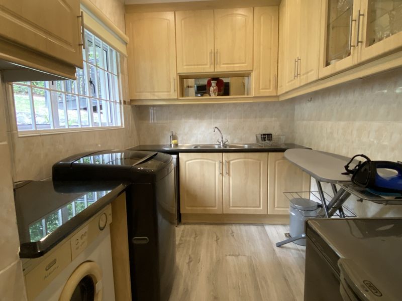 Functional laundry room featuring light wood-finish cabinetry, dark laminate countertops, a stainless steel sink, and tiled backsplash with natural light.