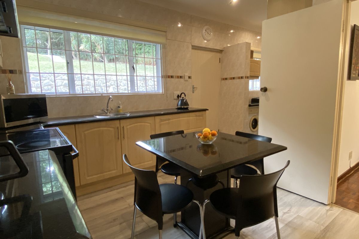 A functional kitchen featuring light wood cabinetry, dark granite countertops, tiled splashbacks, and a dedicated dining area with integrated lighting.