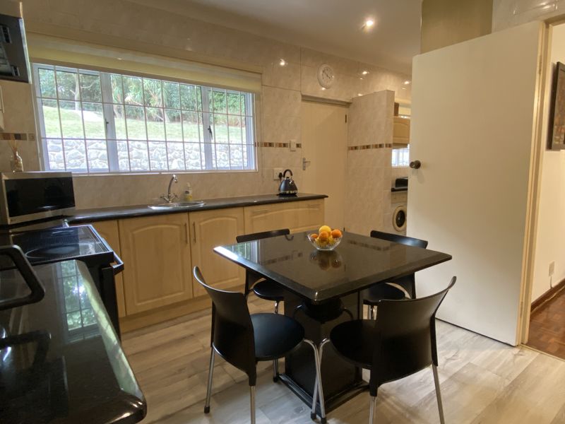 A functional kitchen featuring light wood cabinetry, dark granite countertops, tiled splashbacks, and a dedicated dining area with integrated lighting.