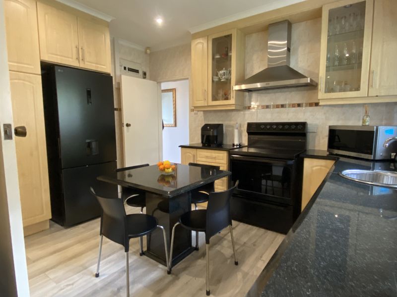 A functional kitchen featuring light wood cabinetry, dark countertops, a stainless steel extractor fan, and modern laminate flooring.