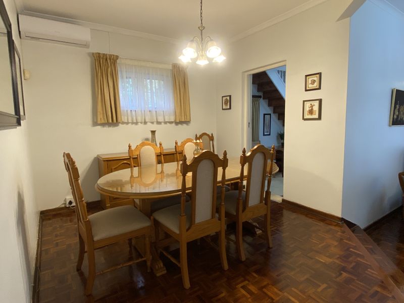 A well-maintained dining room featuring classic parquet flooring, a split-system air conditioner, and a doorway leading to the staircase area.