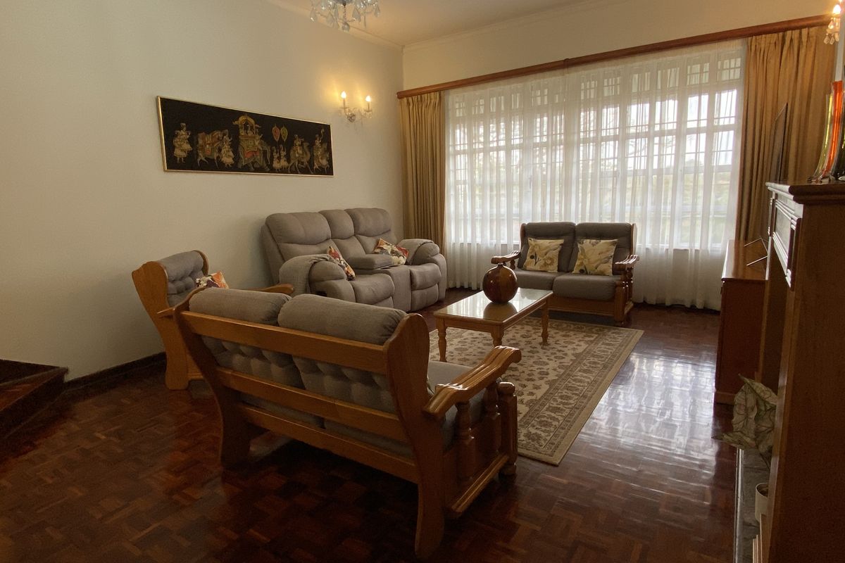 A well-maintained living room featuring polished parquet flooring, a classic crystal chandelier, and large windows that provide ample natural light.