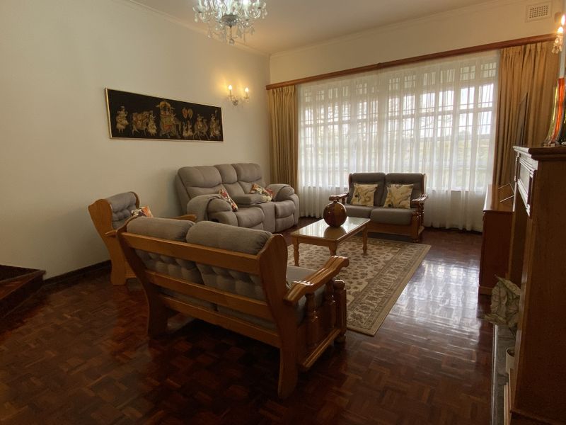 A well-maintained living room featuring polished parquet flooring, a classic crystal chandelier, and large windows that provide ample natural light.