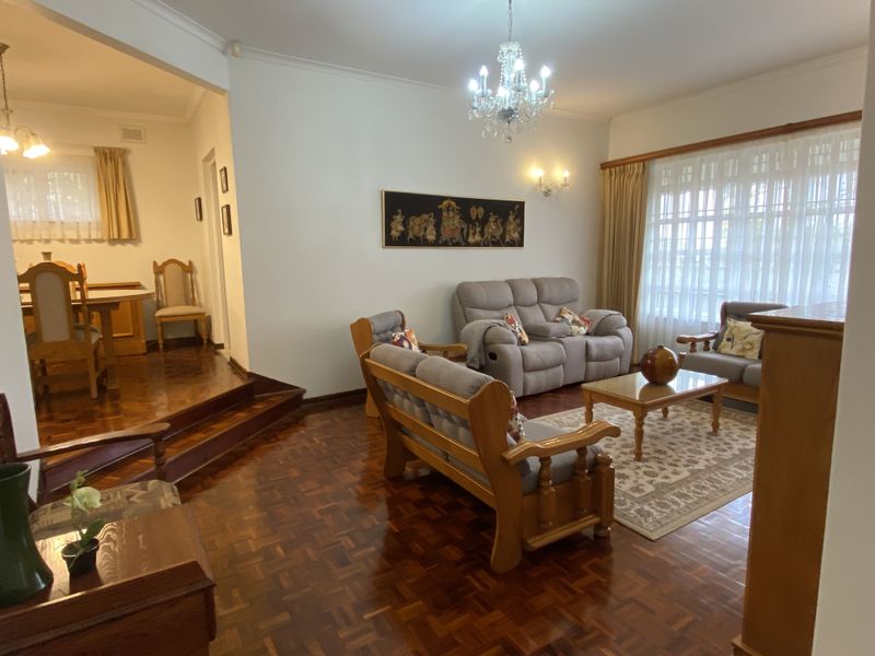 Spacious open-plan living and dining area featuring polished parquet flooring, classic coved cornicing, and a decorative crystal chandelier.