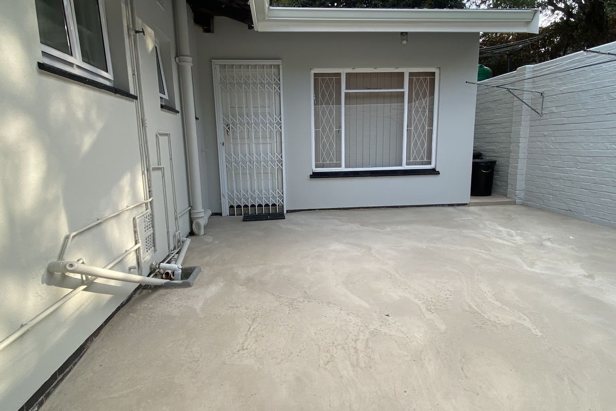 A paved rear courtyard area featuring a security gate, security bars on windows, and exposed exterior plumbing along the side wall.