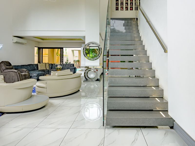 Spacious open-plan living area featuring high ceilings, modern marble-look floor tiles, and a striking stone staircase with a glass balustrade.