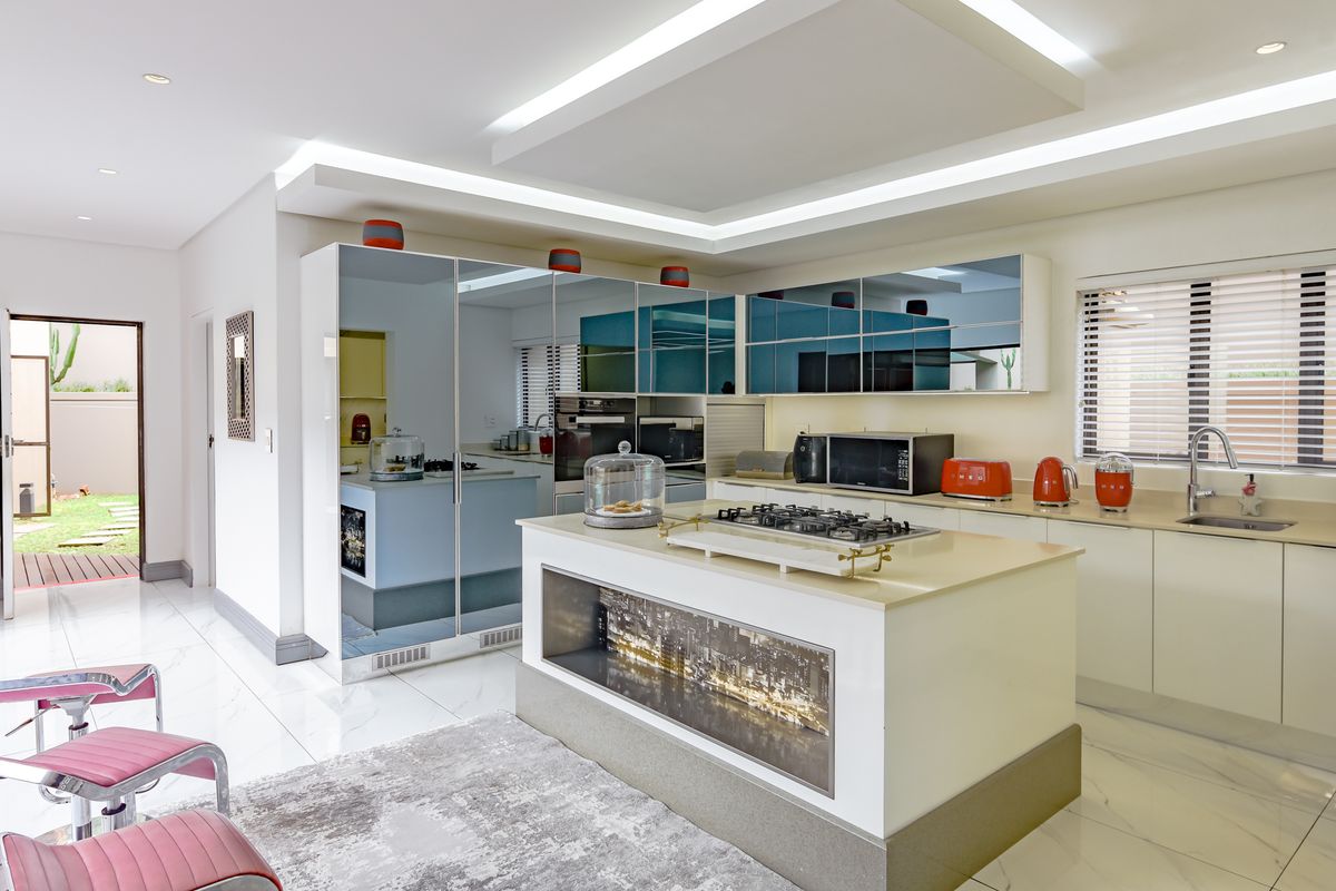 Modern kitchen featuring a central island with gas cooktop, mirrored cabinetry, stone countertops, and integrated appliances, illuminated by recessed ceiling lighting.