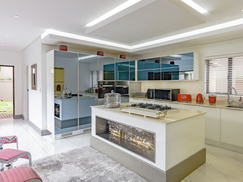 Modern kitchen featuring a central island with gas cooktop, mirrored cabinetry, stone countertops, and integrated appliances, illuminated by recessed ceiling lighting.