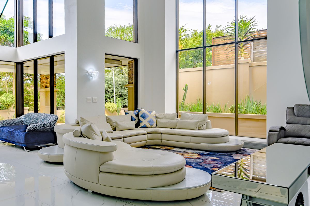 Spacious double-volume living room featuring expansive floor-to-ceiling windows, polished porcelain tile flooring, and seamless access to the outdoor garden area.