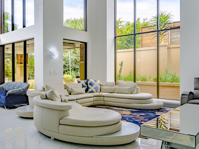 Spacious double-volume living room featuring expansive floor-to-ceiling windows, polished porcelain tile flooring, and seamless access to the outdoor garden area.