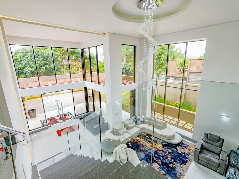 Spacious double-volume living area featuring floor-to-ceiling windows, a modern glass balustrade, and elegant recessed ceiling lighting.