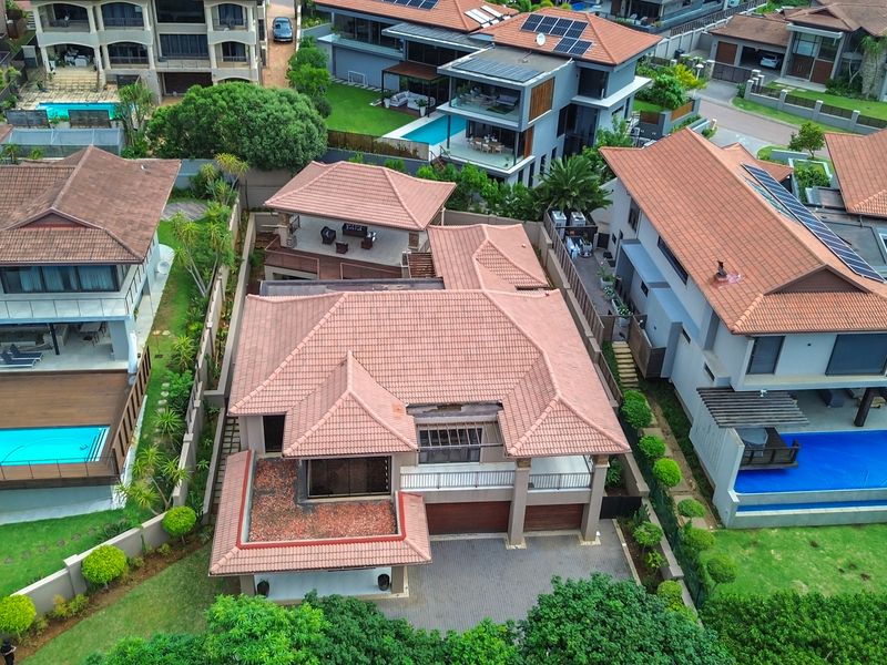 Aerial view of a residential property featuring a tiled roof, paved driveway, and integrated garage, situated within a suburban estate.