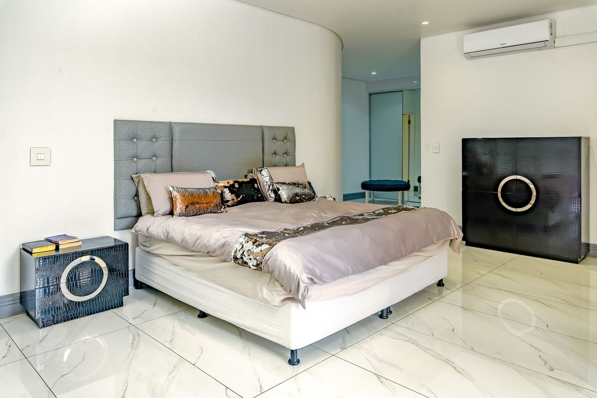 Spacious bedroom featuring polished marble-look floor tiles, a curved architectural wall, and a wall-mounted split-system air conditioner.