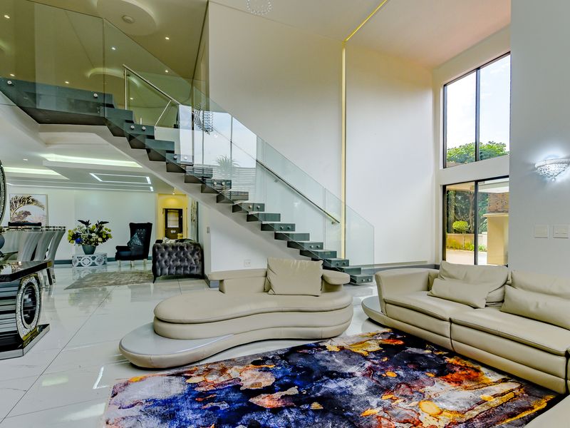 Spacious open-plan living area featuring a striking floating staircase with glass balustrade, double-volume ceilings, and large windows providing abundant natural light.