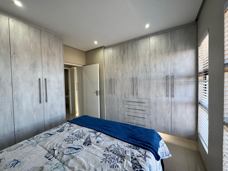 A well-maintained bedroom featuring extensive built-in cupboards with a modern wood-grain finish, recessed lighting, and venetian blinds.