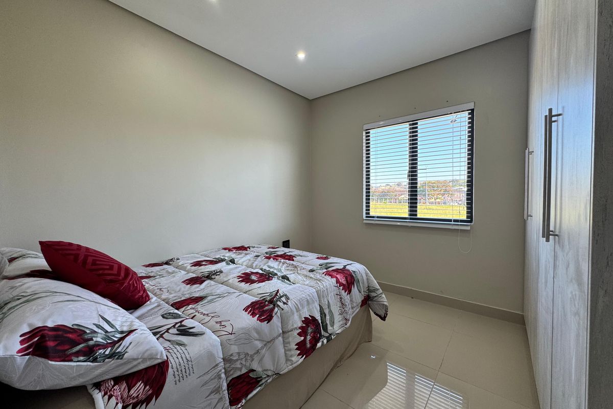A well-maintained bedroom featuring neutral tiled flooring, built-in cupboards, recessed downlighting, and a window with fitted blinds.