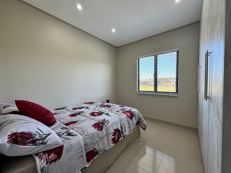A well-maintained bedroom featuring neutral tiled flooring, built-in cupboards, recessed downlighting, and a window with fitted blinds.