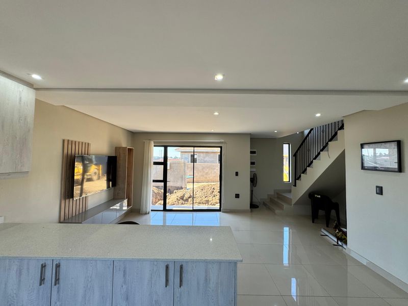 Modern open-plan living area featuring a kitchen island with stone countertops, tiled flooring, recessed lighting, and a staircase with a sleek metal balustrade.
