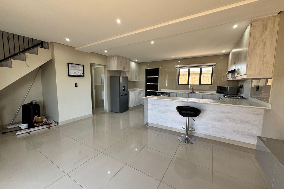 Modern open-plan kitchen featuring light wood-grain cabinetry, stone countertops, integrated hob, and sleek porcelain floor tiles, seamlessly connected to the living area.
