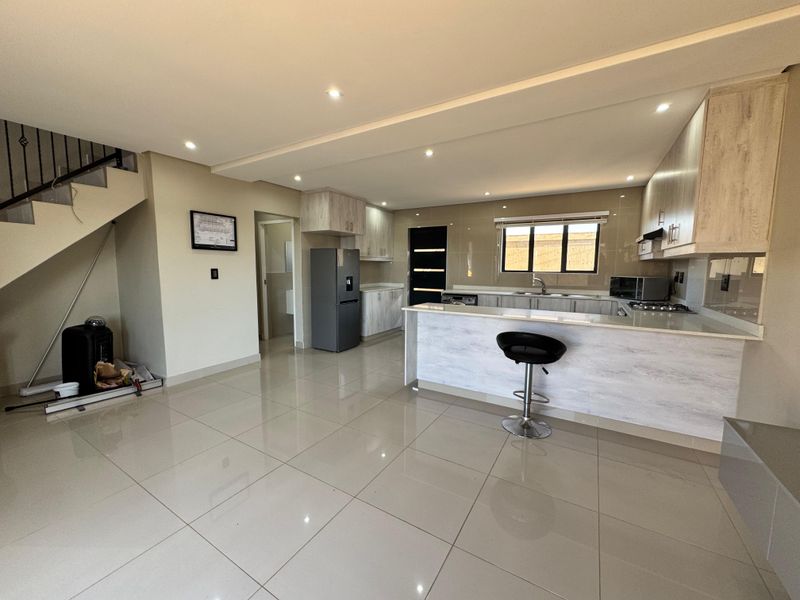 Modern open-plan kitchen featuring light wood-grain cabinetry, stone countertops, integrated hob, and sleek porcelain floor tiles, seamlessly connected to the living area.