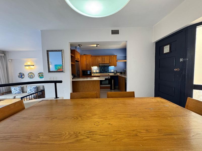 Open-plan dining area adjacent to a functional kitchen featuring wooden cabinetry, integrated appliances, and a tiled backsplash.
