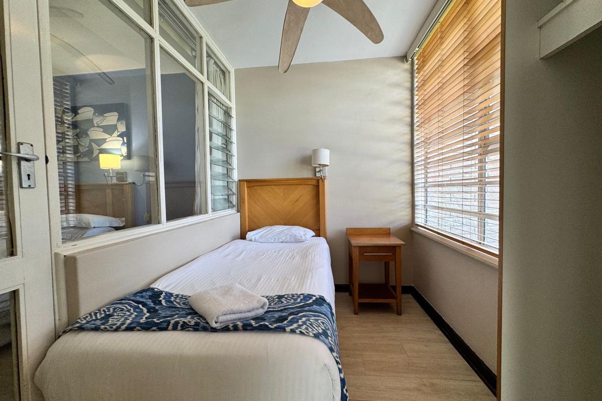 A compact bedroom featuring laminate flooring, a ceiling fan, and an internal glass partition wall allowing natural light flow.
