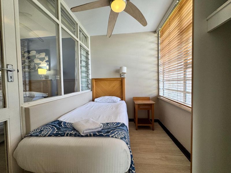 A compact bedroom featuring laminate flooring, a ceiling fan, and an internal glass partition wall allowing natural light flow.