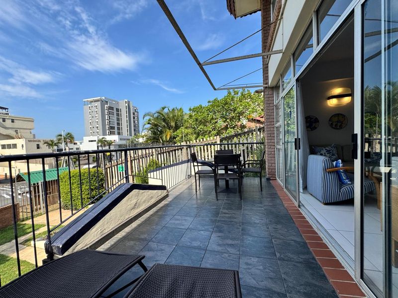 A spacious balcony featuring tiled flooring, a metal safety railing, and large sliding glass doors providing seamless access to the interior living area.