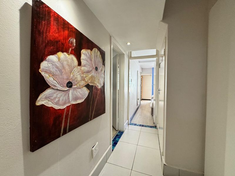 A bright, tiled hallway featuring recessed downlighting and clean white finishes, providing access to multiple rooms within the apartment.