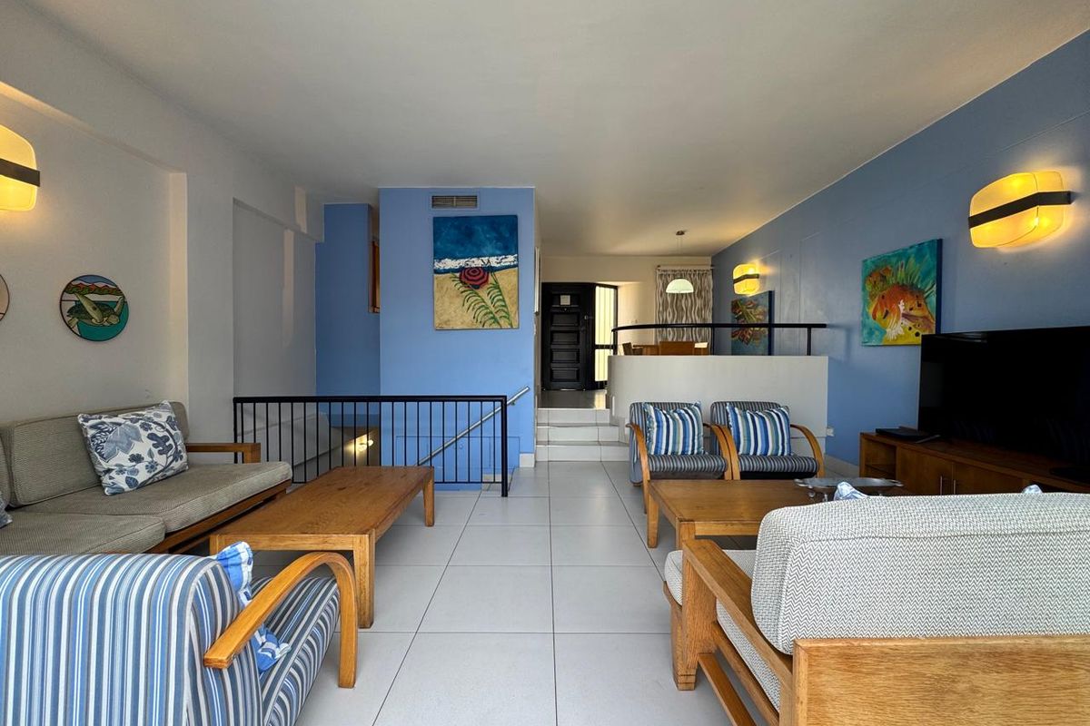 A split-level living room featuring tiled flooring, blue accent walls, and a metal stair railing leading to the entrance area.