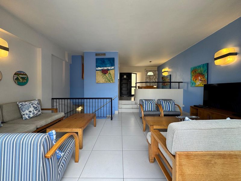 A split-level living room featuring tiled flooring, blue accent walls, and a metal stair railing leading to the entrance area.
