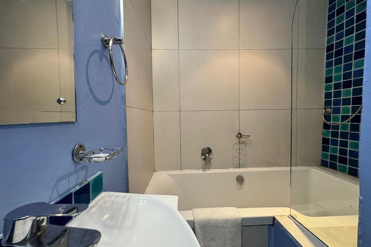 A functional bathroom featuring a bathtub with a shower screen, vanity basin, and decorative mosaic tile accents.