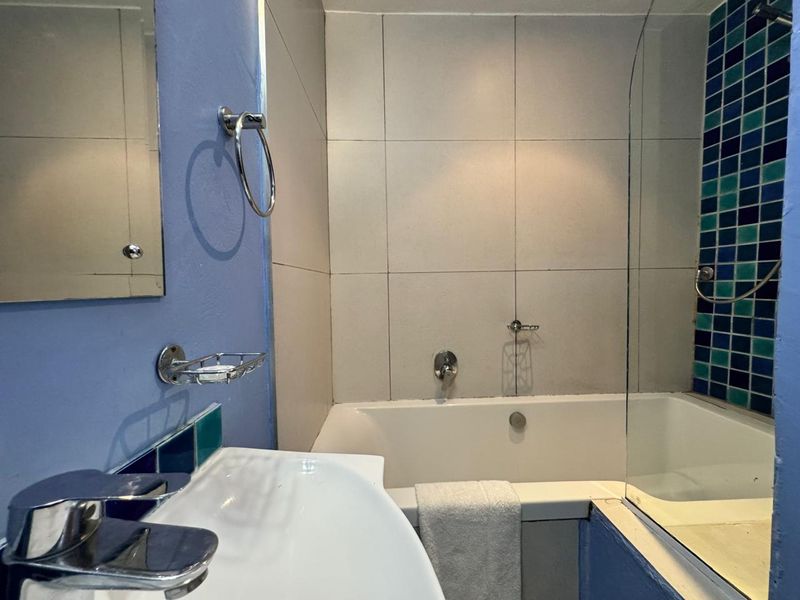 A functional bathroom featuring a bathtub with a shower screen, vanity basin, and decorative mosaic tile accents.