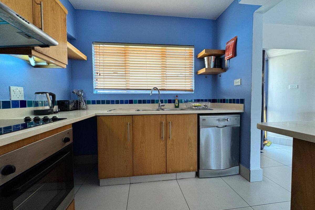 A functional kitchen featuring wooden cabinetry, tiled splashbacks, built-in oven, hob, extractor fan, and integrated dishwasher with tiled flooring.